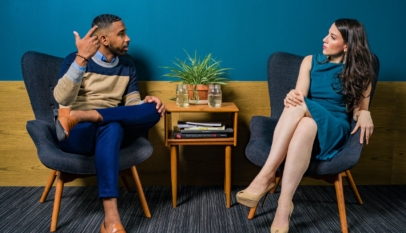 woman wearing teal dress sitting on chair talking to man